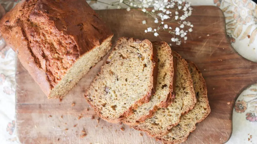 A sliced loaf of banana bread on a wooden cutting board. 