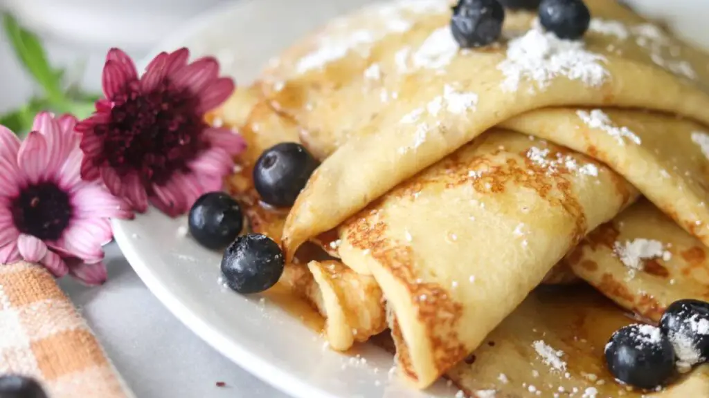 A plate of sourdough crepes with fresh blueberries and powdered sugar on top.