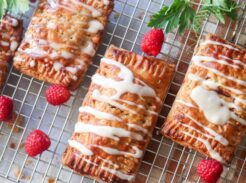 Homemade raspberry pop tarts on a cooling rack with fresh raspberries.