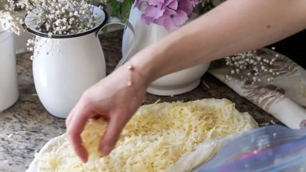 Sprinkling cheese onto a flattened ball of bread dough.