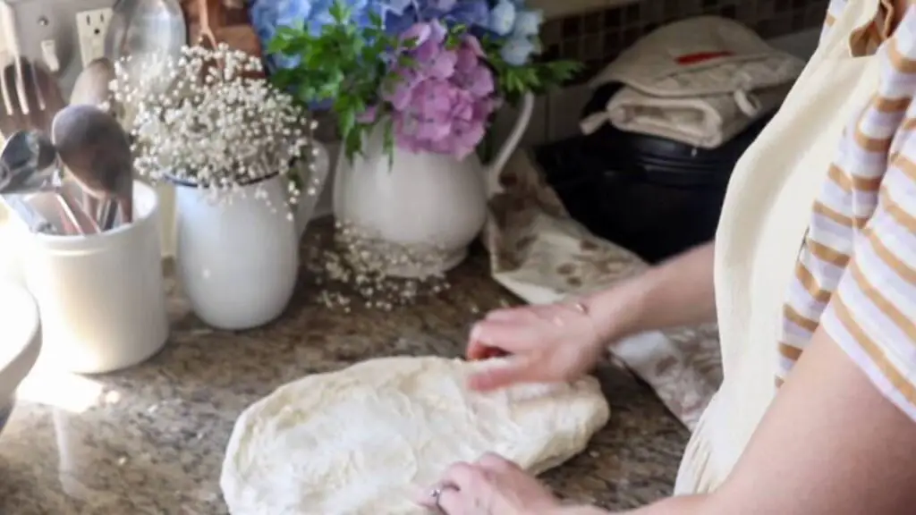 Flattening a ball of bread dough on a counter.