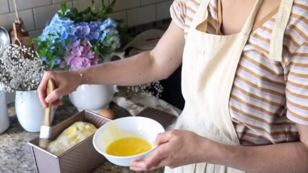 Brushing a loaf of bread with egg wash.