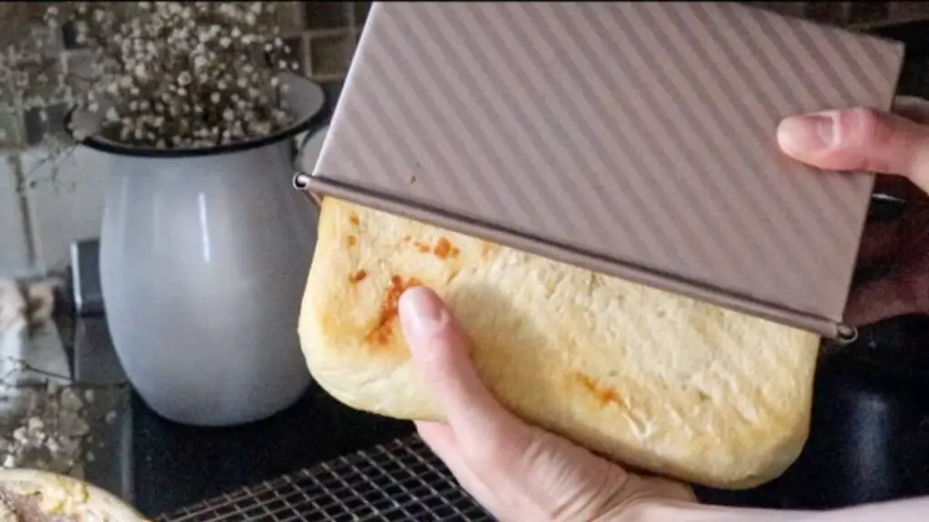 Pulling a loaf of bread out of a bread pan.