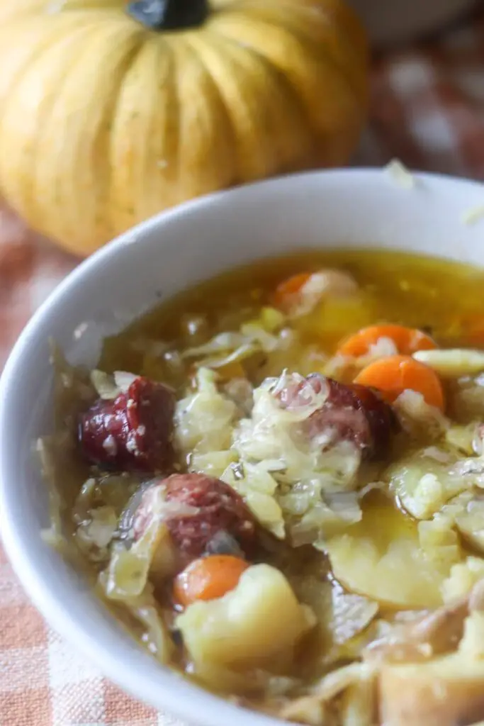 A bowl of bratwurst cabbage soup with a pumpkin in the background.