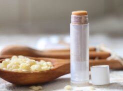 A tube of pumpkin lip balm with a spoonful of beeswax pellets in the background.