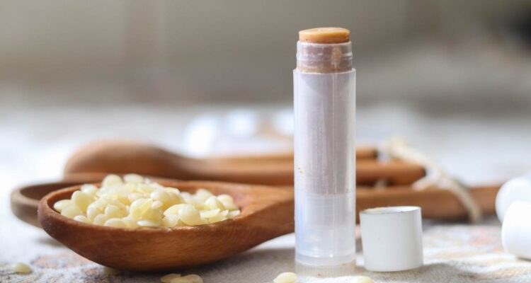 A tube of pumpkin lip balm with a spoonful of beeswax pellets in the background.