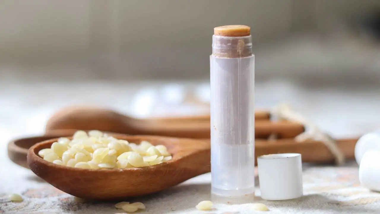 A tube of pumpkin lip balm with a spoonful of beeswax pellets in the background.