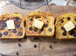 Three pieces of french toast on a wooden cutting board with butter and chocolate chips.