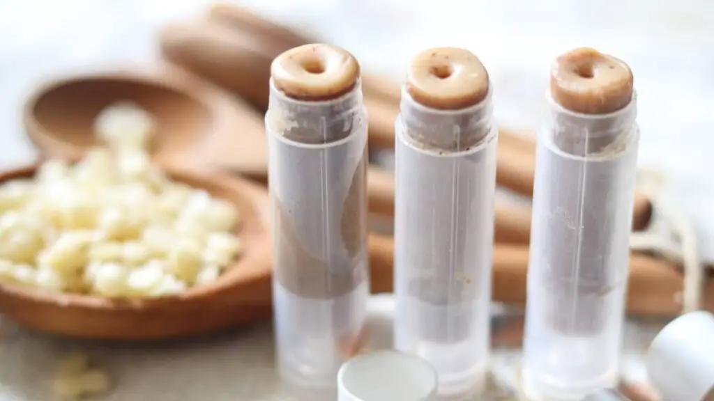 Three pumpkin lip balm tubes with beeswax in the background.