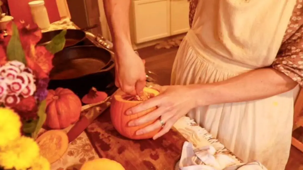 Using a spoon to scoop the guts and seeds out of a small pumpkin.