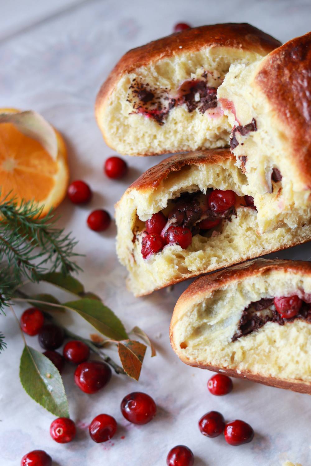 Cranberry chocolate brioche rolls lined up next to fresh cranberries and orange slices.