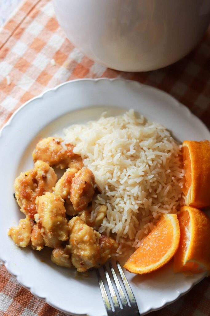 Orange chicken on a white plate with rice and orange slices.