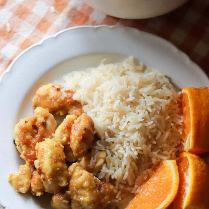 Orange chicken on a white plate with rice and orange slices.