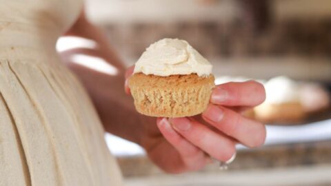 Holding a frosted vanilla cupcake.