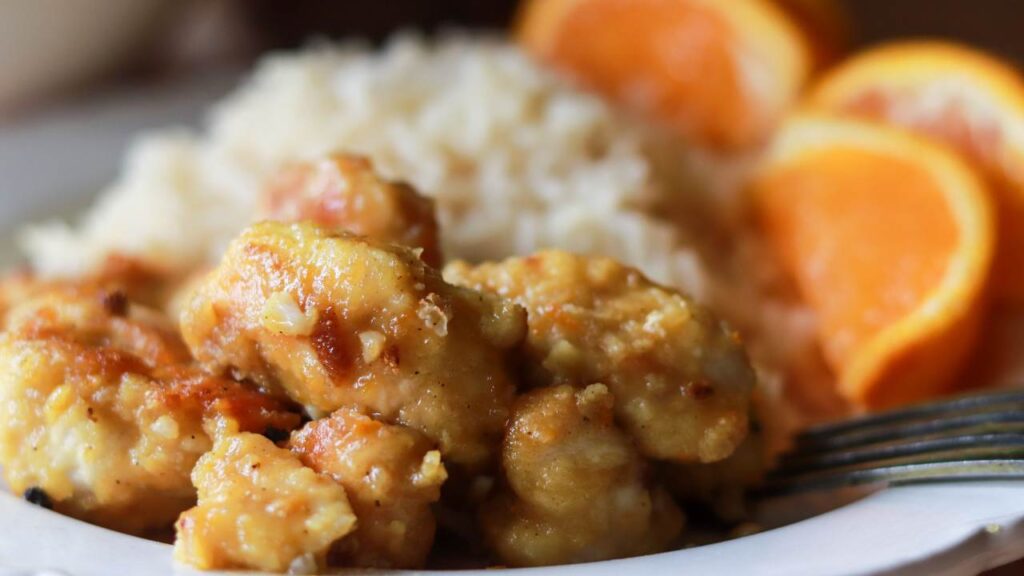 Health orange chicken on a white plate with rice and orange slices.