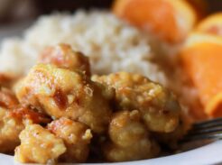 Health orange chicken on a white plate with rice and orange slices.