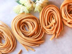 Four rolls of homemade pasta lined up on a table with fresh flowers.