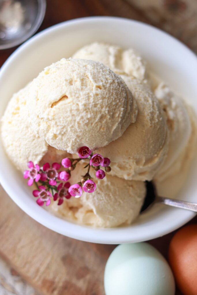 Looking down on a bowl of vanilla ice cream scoops with fresh eggs beside it.