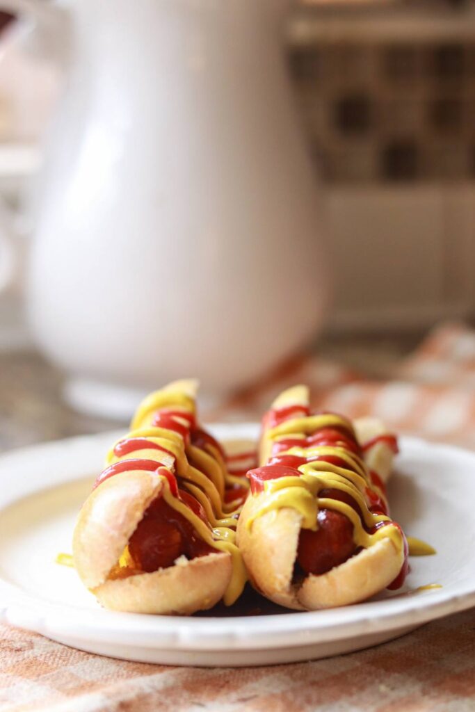 A plate with two hot dogs drizzled with mustard and ketchup.