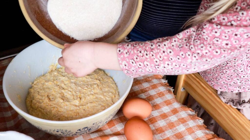 A little girl helping mix cornbread batter in a large mixing bowl.