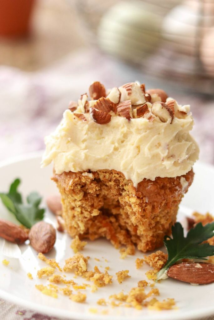 a carrot cake cupcake with cream cheese icing and topped with chopped nuts sitting on a small plate.