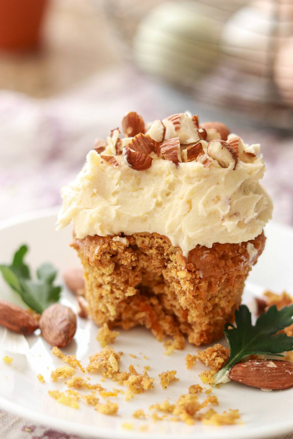 a carrot cake cupcake with cream cheese icing and topped with chopped nuts sitting on a small plate.