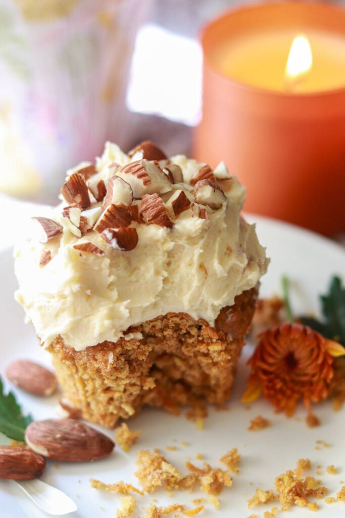 a carrot cake cupcake sitting on a small place with a bite taken from it.