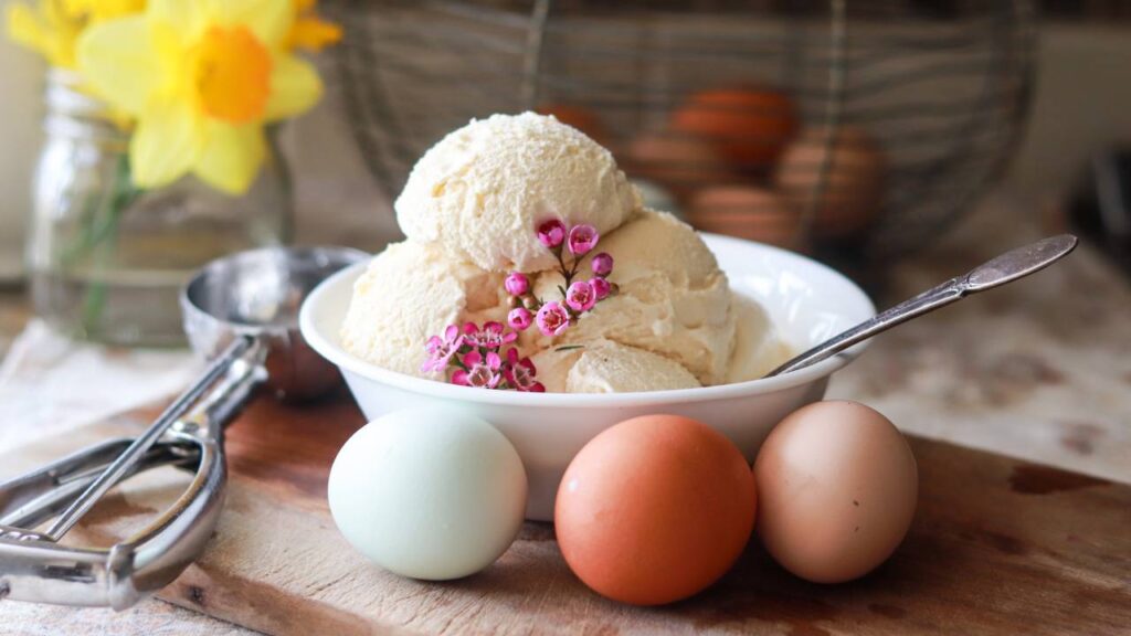 A bowl of homemade vanilla ice cream with fresh eggs and an ice cream scoop.