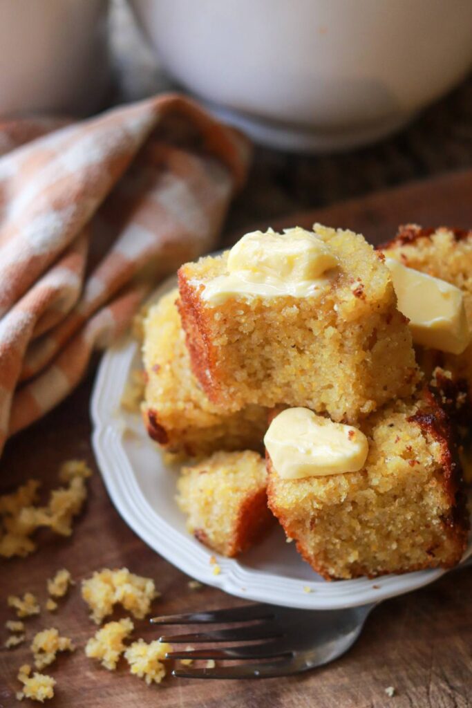 A plate of cornbread with pads of butter on each slice.