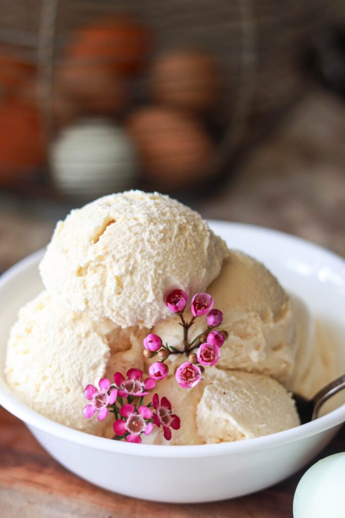 A bowl of homemade vanilla ice cream with pink flowers.