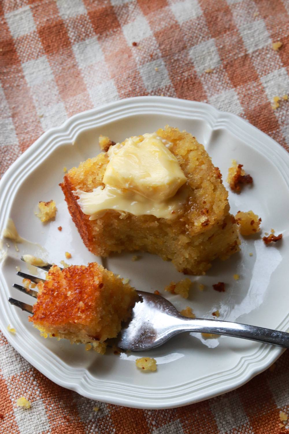 A piece of cornbread with butter and a fork taking a bite.