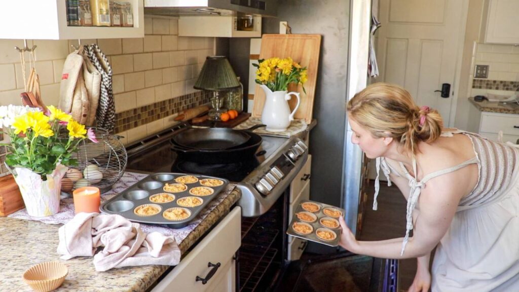 a woman putting a small cupcake pan into the oven to bake.