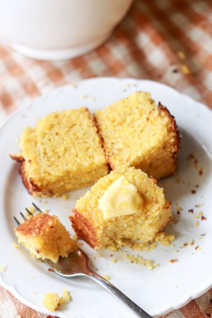 Three pieces of cornbread on a white plate with a fork.