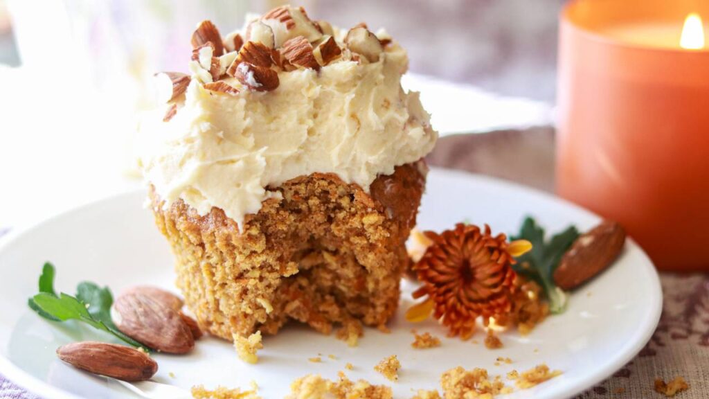 a carrot cake cupcake sitting on a small plate with a bite taken out.