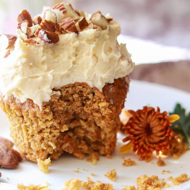 a carrot cake cupcake sitting on a small plate with a bite taken out.