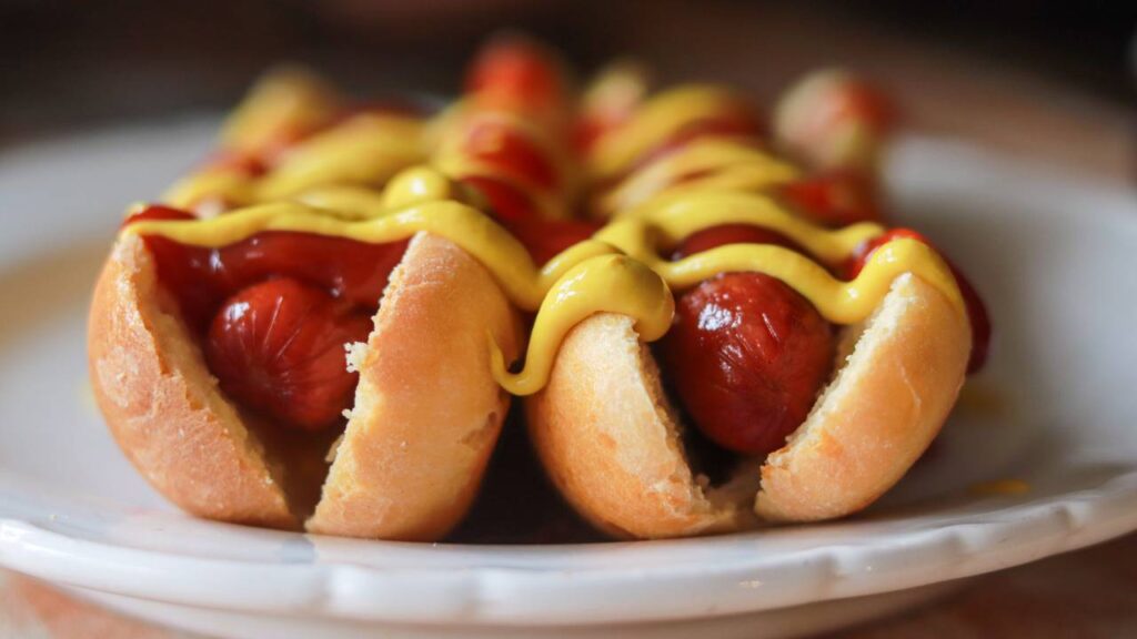 Two hot dogs sitting on a plate with mustard and ketchup.
