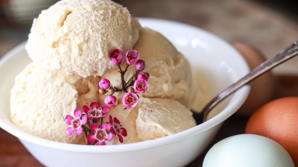 A bowl of homemade vanilla ice cream with fresh eggs next to it.