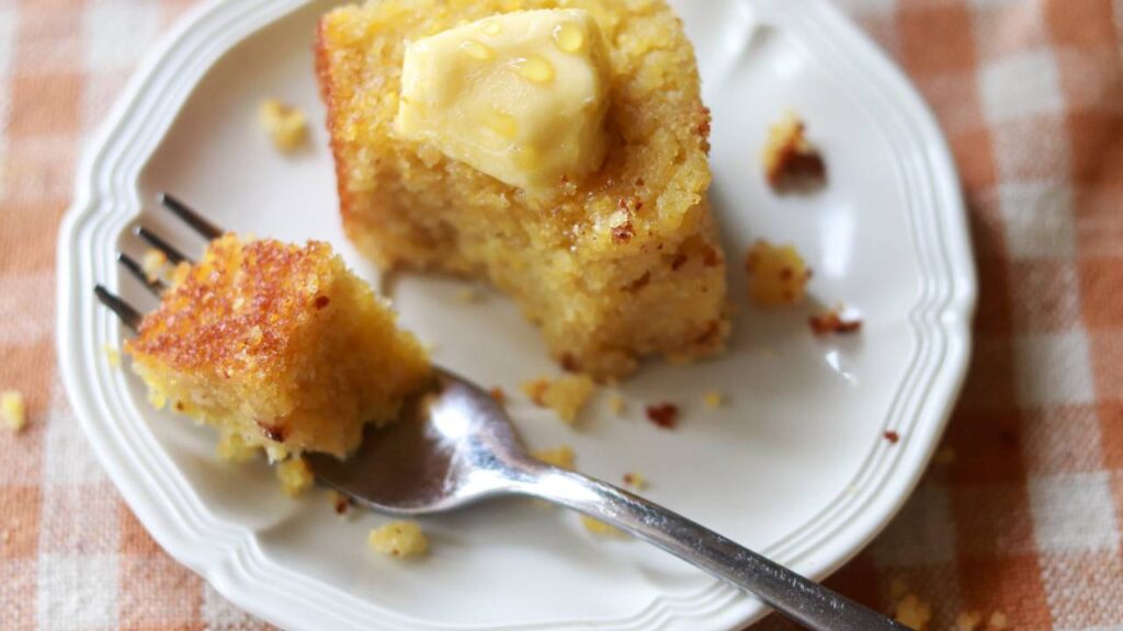 A piece of cornbread with butter and a fork taking a bite out of it.