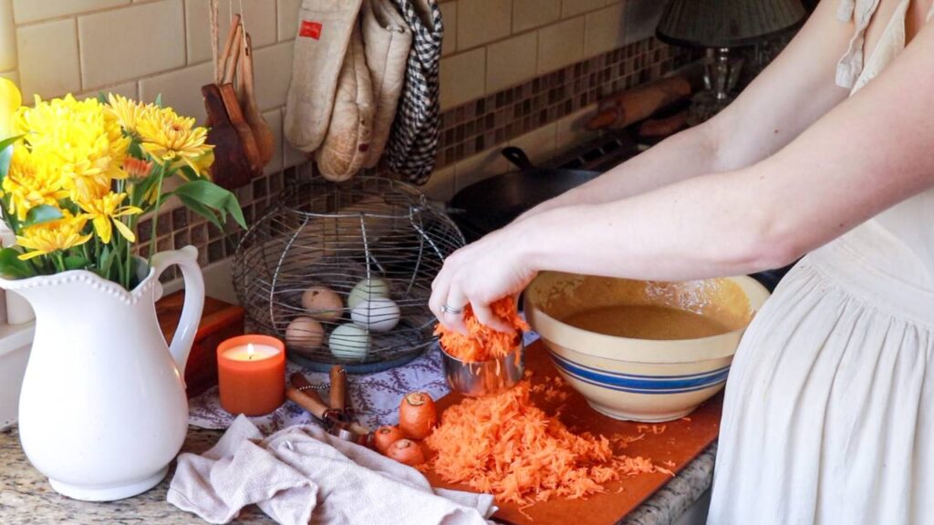 a woman measuring out shredded carrots to put in a mixing bowl with cupcake mix.