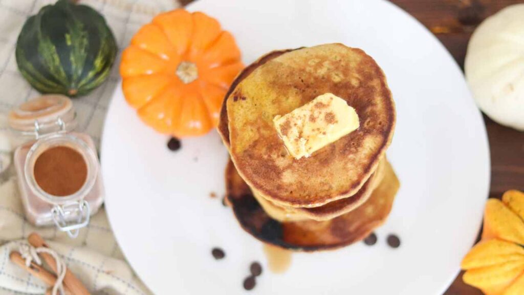Stack of sourdough discard pumpkin pancakes topped with butter, on a plate with a small decorative pumpkin.