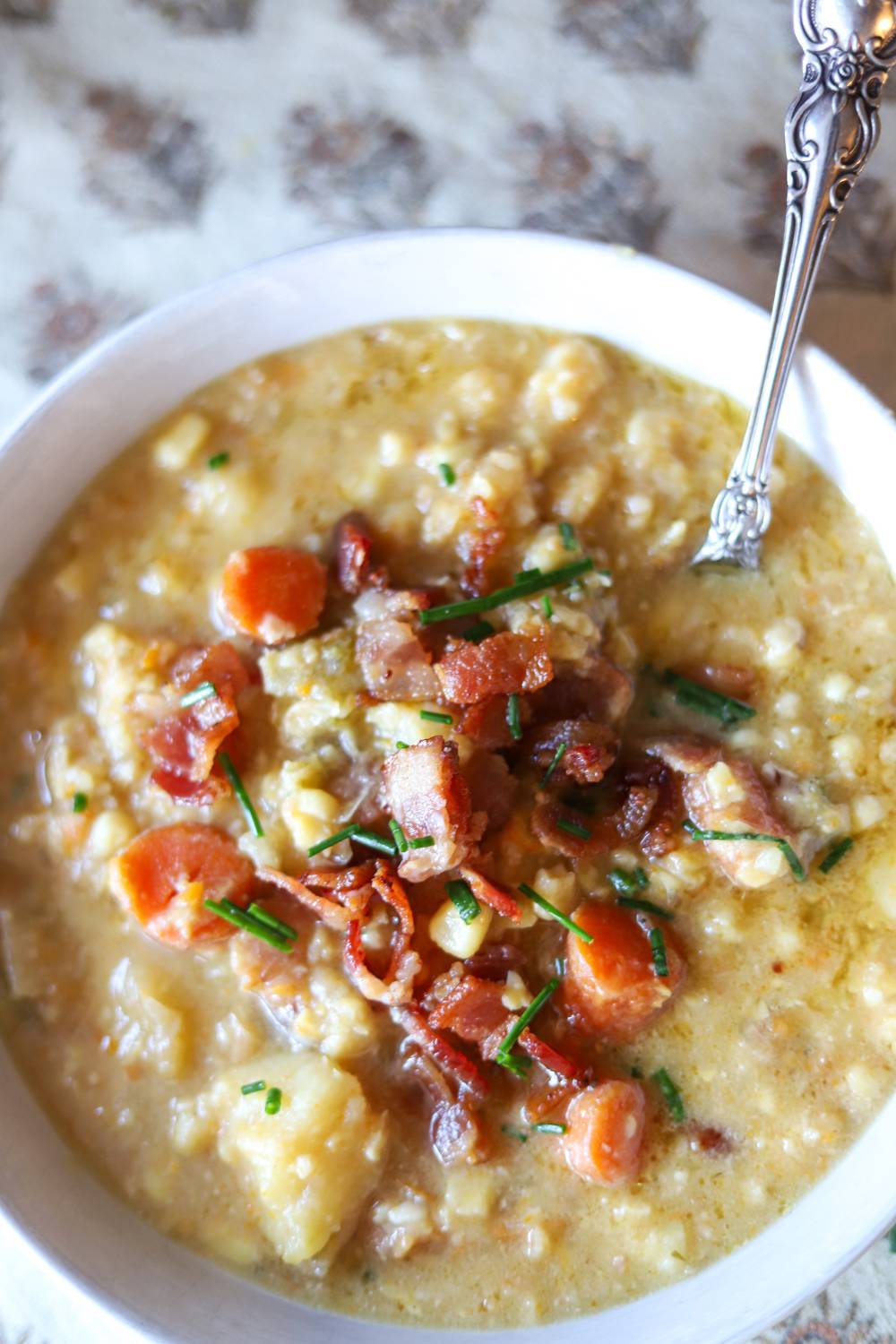 Bowl of creamy corn chowder topped with crispy bacon and chopped chives.