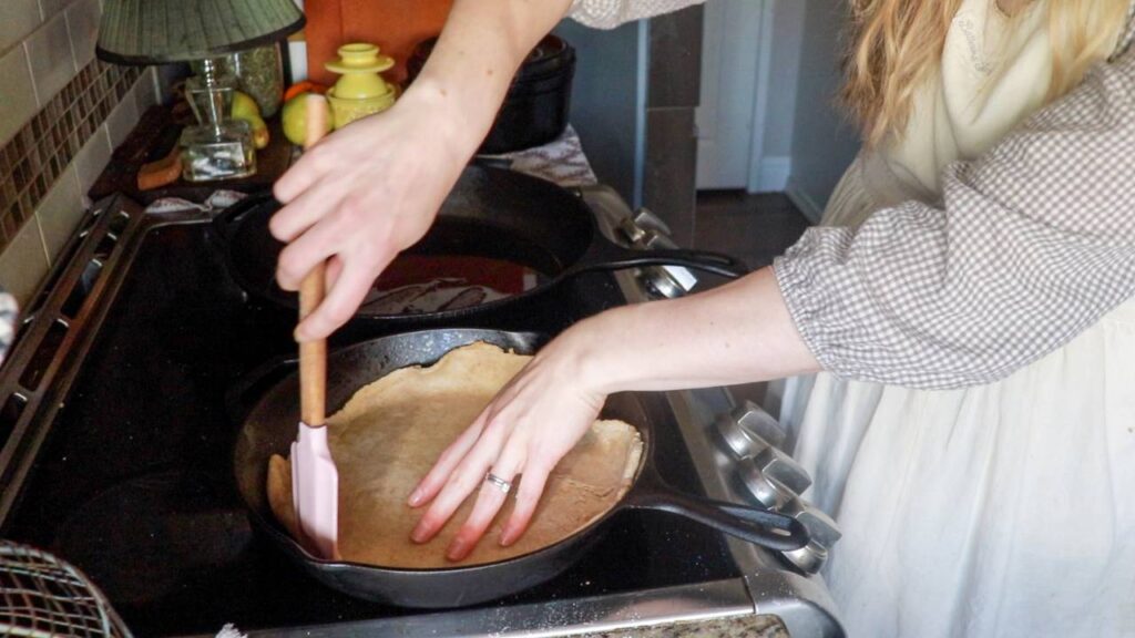 Hands pressing sourdough pizza dough into a cast iron skillet on a stovetop, preparing the crust for baking.