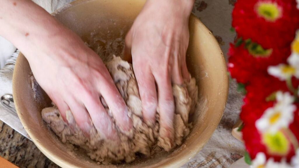 Hands kneading sourdough pizza dough in a large mixing bowl.