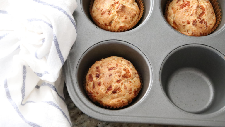Fluffy cheesy sourdough discard biscuits in a muffin tin with a white and blue kitchen towel