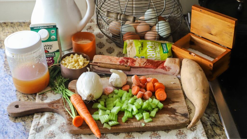 Ingredients for corn chowder on a cutting board, including vegetables, bacon, and corn.