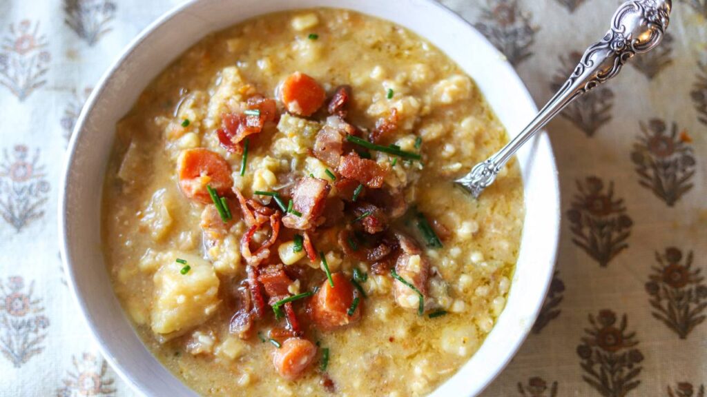 Bowl of creamy corn chowder topped with crispy bacon and chopped chives.