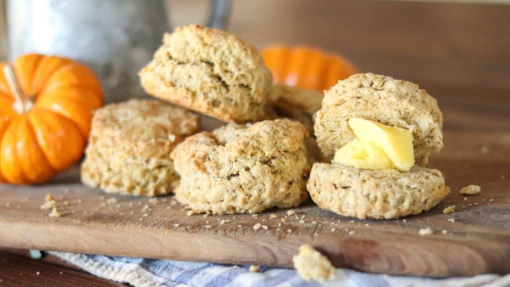 Sourdough discard pumpkin biscuits on a wooden board, with one biscuit split open and topped with butter.