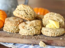 Sourdough discard pumpkin biscuits on a wooden board, with one biscuit split open and topped with butter.