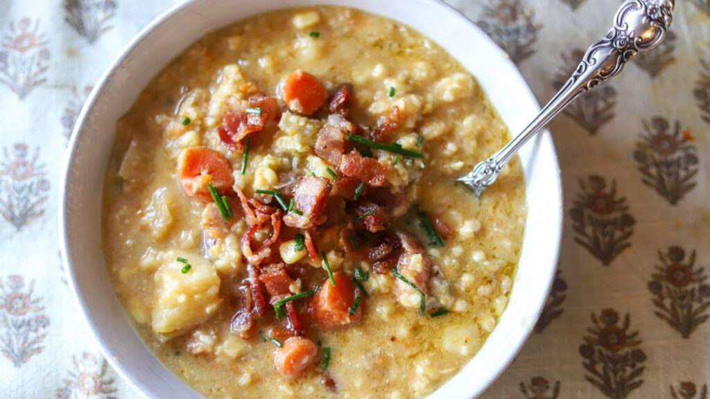 Bowl of creamy corn chowder topped with crispy bacon and chopped chives.