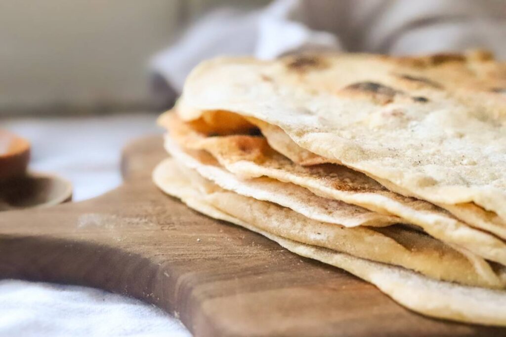 Stack of homemade einkorn sourdough discard tortillas on a wooden cutting board.